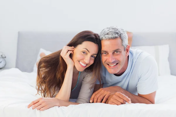 Casal deitado na cama e sorrindo para a câmera — Fotografia de Stock