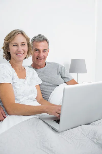 Pareja de mediana edad usando su portátil juntos en la cama —  Fotos de Stock