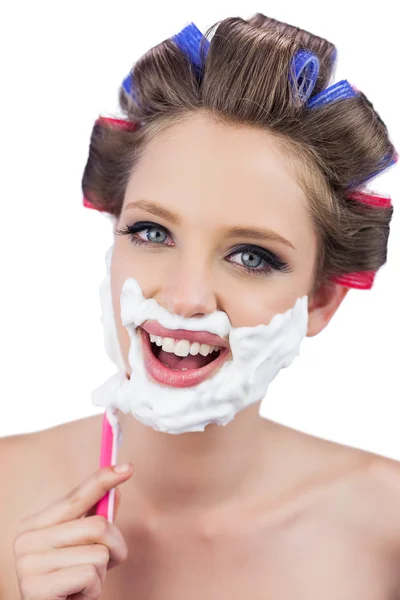 Smiling model in hair curlers posing while shaving — Stock Photo, Image