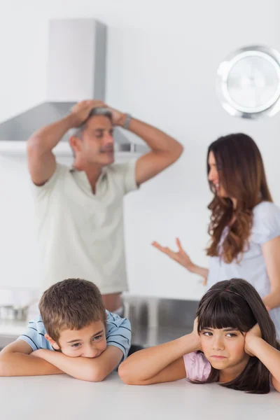 Unhappy siblings sitting in kitchen with their parents who are a — Stock Photo, Image