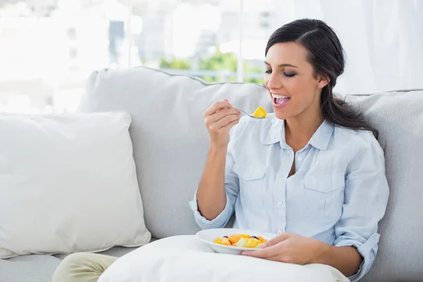 Žena uvolňující na gauči, jíst ovocný salát — Stock fotografie