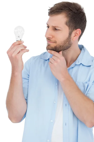 Sceptical model holding a bulb and touching his chin — Stock Photo, Image