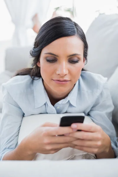 Женщина с темными волосами лежит на диване и отправляет сообщения. — стоковое фото