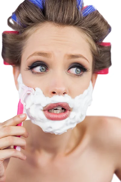 Shocked young model in hair curlers posing with razor — Stock Photo, Image