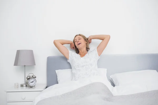 Mujer rubia bien descansada estirándose y bostezando en la cama —  Fotos de Stock