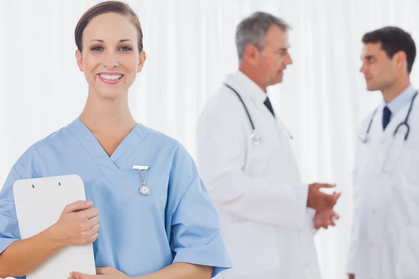 Smiling surgeon posing while doctors talking on background — Stock Photo, Image