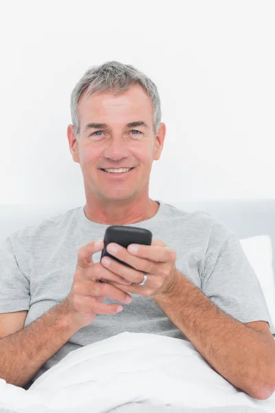 Happy grey haired man sending a text in bed — Stock Photo, Image