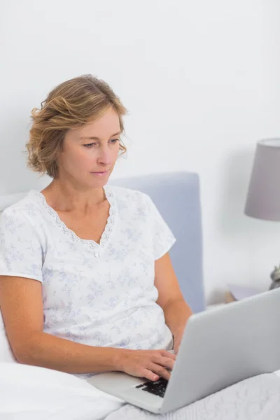 Donna bionda seduta a letto con il computer portatile — Foto Stock