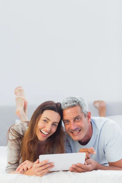 Happy couple lying on bed using their tablet pc — Stock Photo, Image