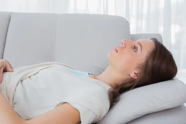 Upset brunette with a vacant look lying on the couch — Stock Photo, Image