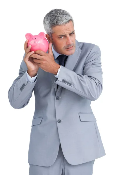 Sceptical businessman holding piggy bank — Stock Photo, Image