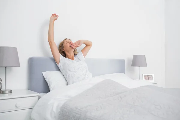 Mujer rubia estirándose y bostezando en la cama por la mañana —  Fotos de Stock