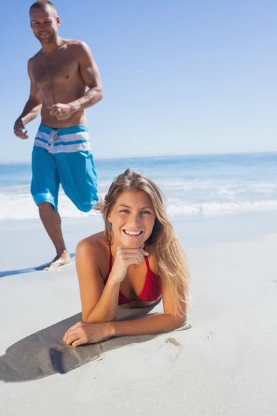 Lächelnde Frau, die auf dem Sand liegt, während Mann zu ihr kommt — Stockfoto