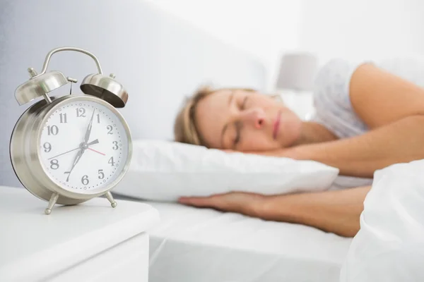 Mujer rubia dormida en la cama mientras su alarma muestra la hora temprana — Foto de Stock