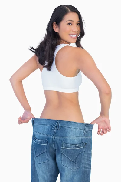 Woman holding her too big jeans smiling at camera — Stock Photo, Image