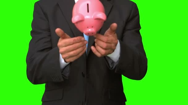 Geschäftsmann wirft Sparschwein auf grünen Bildschirm — Stockvideo