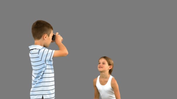 Brother taking pictures of his sister jumping on grey screen — Stock Video