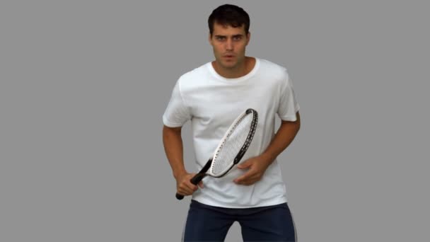 Hombre guapo entrenando mientras juega al tenis en pantalla gris — Vídeos de Stock