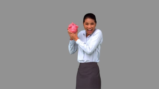 Businesswoman shaking a full piggy bank on grey screen — Stock Video