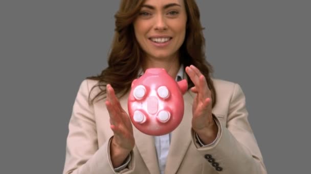 Businesswoman throwing a piggy bank on grey screen — Stock Video