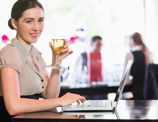 Happy businesswoman holding wine glass using laptop and looking at camera — Stock Photo, Image