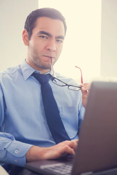 Irritated man biting his eyeglasses and using a laptop — Stock Photo, Image