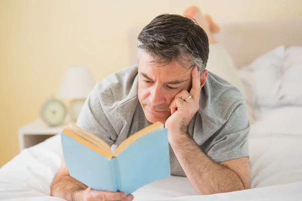 Homem concentrado lendo um livro em sua cama — Fotografia de Stock