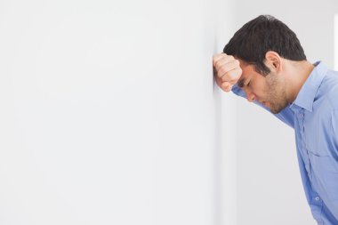 Angry man leaning his head against a wall clipart