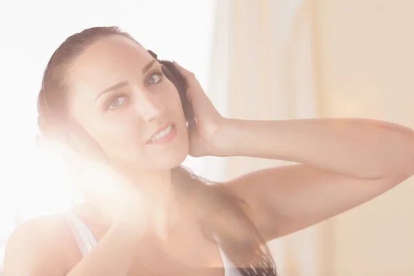 Smiling brunette sitting on bed listening to music — Stock Photo, Image