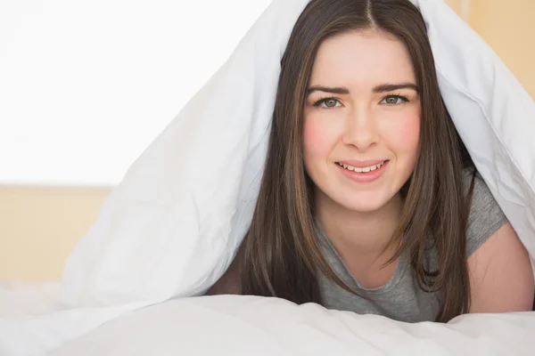 Smiling girl looking at camera lying in her bed — Stock Photo, Image