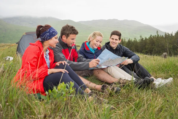 Amigos sentados en la hierba y mirando el mapa en el viaje de camping — Foto de Stock