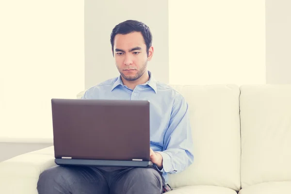 Скучный человек, сидящий на диване с ноутбуком — стоковое фото