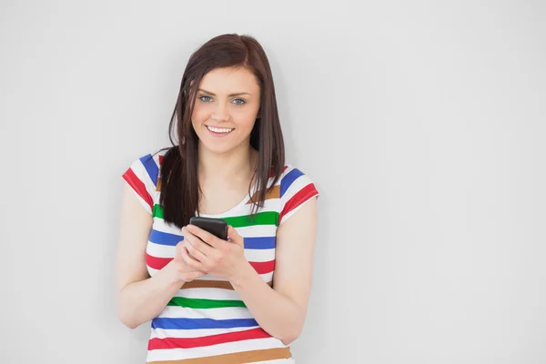 Usmívající se dívka pomocí svého mobilního telefonu při pohledu na fotoaparát — Stock fotografie