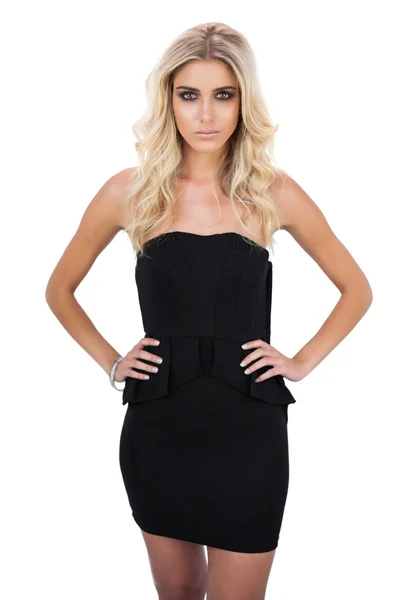 Lächelndes blondes Model im schwarzen Kleid posiert mit den Händen auf den Hüften — Stockfoto