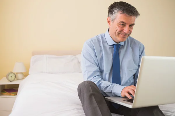 Hombre contento usando un portátil sentado en una cama —  Fotos de Stock