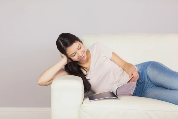 Pretty asian girl lying on the sofa reading a magazine — Stock Photo, Image