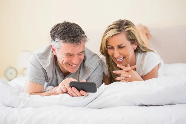 Happy couple lying on a bed and watching a mobile phone — Stock Photo, Image