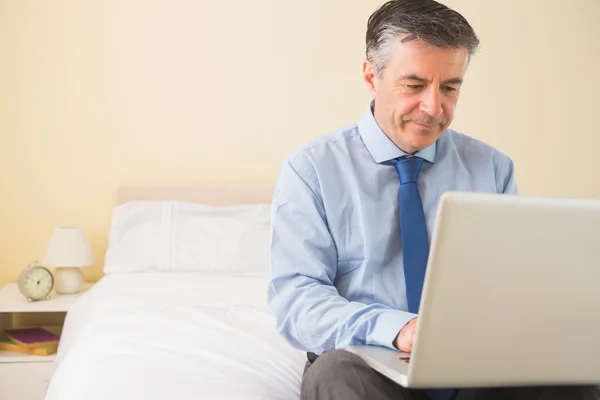 Thoughtful man using a laptop sitting on a bed — Stock Photo, Image