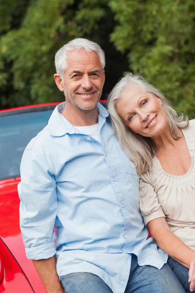 Cheerful mature couple sitting on their red convertible — Stock Photo, Image