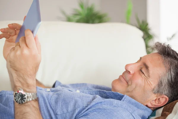 Uomo sorridente sdraiato su un divano utilizzando un tablet pc — Foto Stock