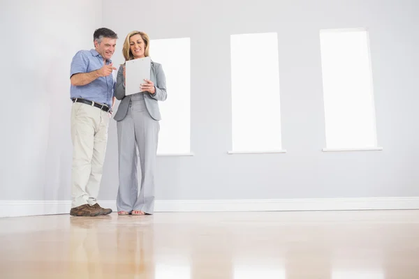 Cheerful blonde realtor showing a room and some documents to a potential attentive buyer — Stock Photo, Image