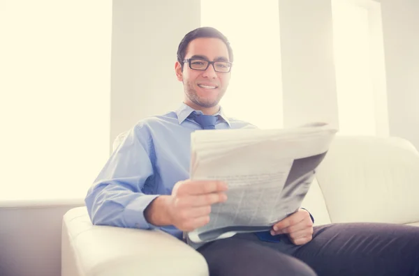 Hombre agradable mirando a la cámara y sosteniendo un periódico sentado en un sofá — Foto de Stock