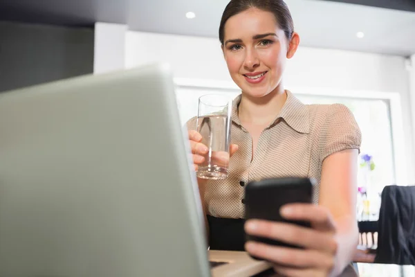 Smiling businesswoman holding glass of water and phone in a cafe — Stock Photo, Image