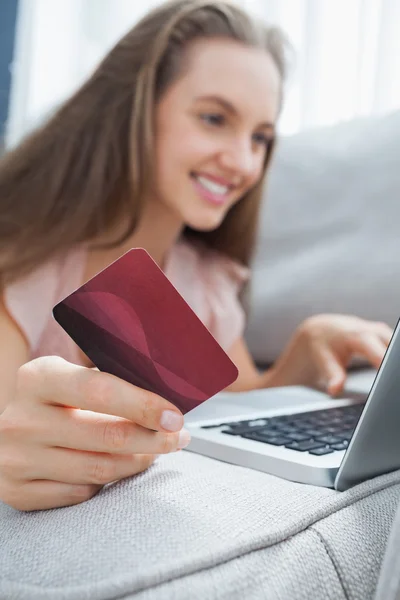 Lachende vrouw liggen ona bank holding een kaart en laptop — Stockfoto