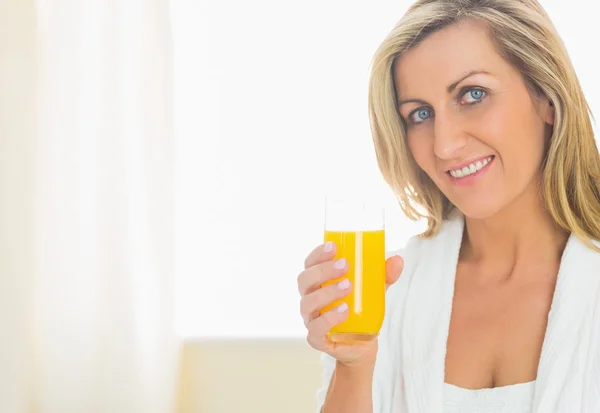 Mujer satisfecha mirando a la cámara disfrutando de un vaso de jugo de naranja —  Fotos de Stock