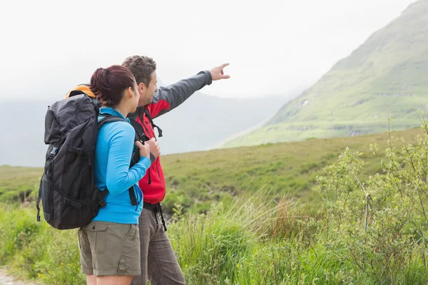 Pareja de excursionistas con mochilas apuntando a la montaña —  Fotos de Stock