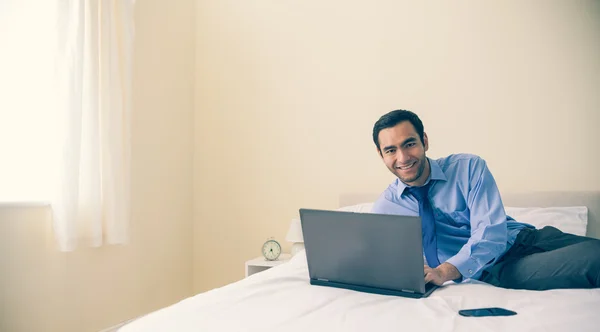 Content man lying on a bed using a laptop — Stock Photo, Image