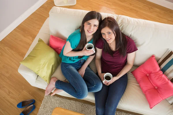两个快乐朋友喝咖啡，坐在沙发上看着相机 — 图库照片