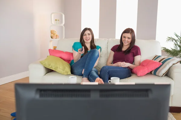 Två vackra vänner på soffan tittar på tv tillsammans — Stockfoto