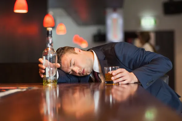 Unmoving businessman holding whiskey glass lying on a counter — Stock Photo, Image